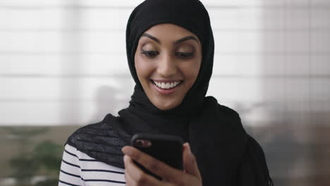 Primer-Plano-Retrato-De-Una-Joven-Mujer-De-Negocios-Musulmana-Riendo-Alegre-Disfrutando-Viendo-Videos-Usando-Un-Teléfono-Inteligente-En-El-Fondo-De-La-Oficina-Diversión-En-El-Trabajo