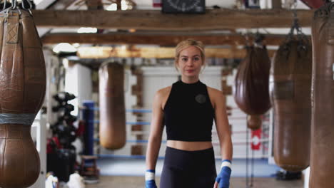 Retrato-De-Boxeadora-En-El-Gimnasio-Caminando-Hacia-La-Cámara-Pasando-Por-Sacos-De-Boxeo-Antiguos