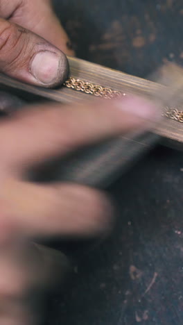 cu shot: young jeweler grinds new golden bracelet with rasp on wooden gutter at dark table in workshop close view