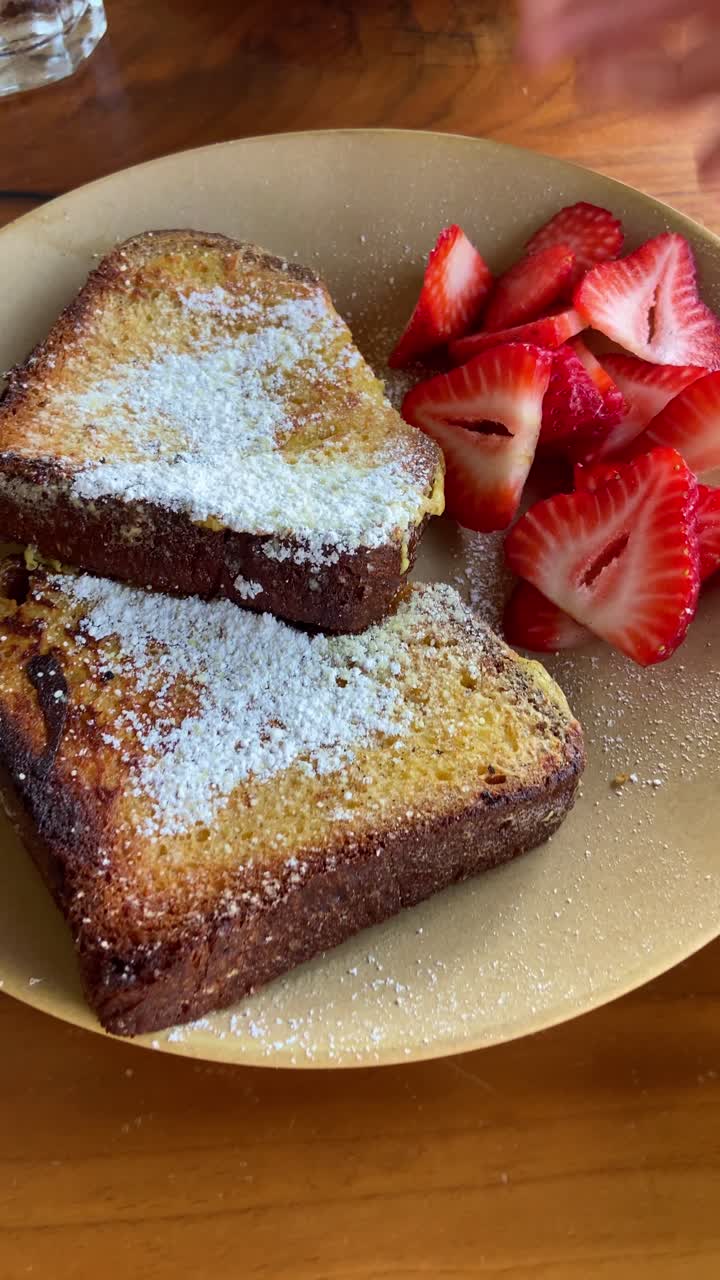 Delicious french toast and strawberries plate is served on table filmed from phone pov of food vlogger or critic. Social media content style or user generated. Tasty food in cafe or breakfast bistro