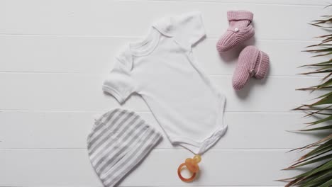 Video-of-white-baby-grow,-hat,-dummy-and-pink-booties-with-copy-space-on-white-background