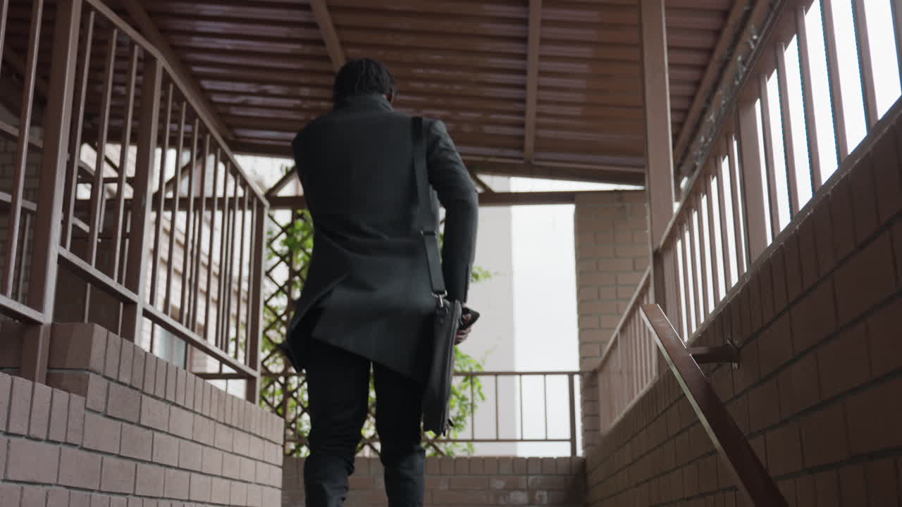 Dark skinned chap walks back toward door in clean hallway, casual pace, calm posture, glances at entry, home interior mood, quiet corridor, everyday life moment of return, privacy and solitude vibe