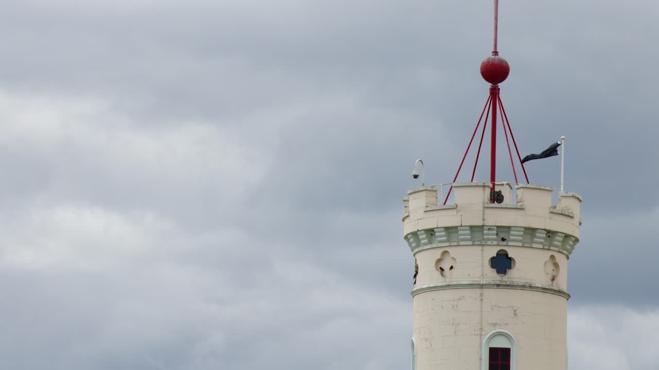 Red time ball ascends atop lighthouse tower under cloudy sky, static camera, natural daylight