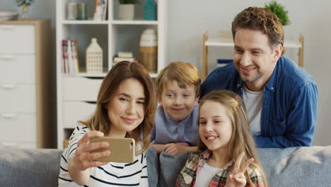 padres, hija e hijo, sentados en el sofá de casa haciendo divertidos selfies en el smartphone, sonriendo y posando para la cámara