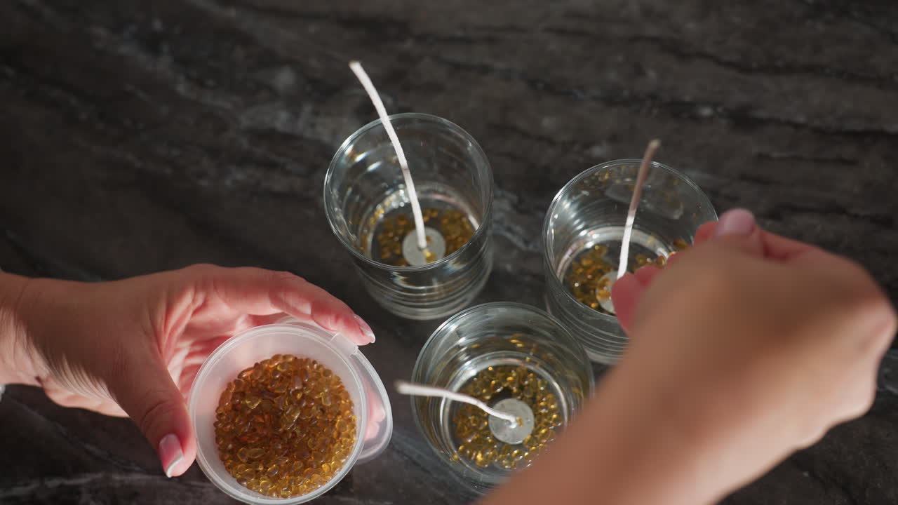 Aerial view of person pouring brown color beads into glass cup for design work, showing process of organizing materials and adding decorative beads into cups for creative project setup