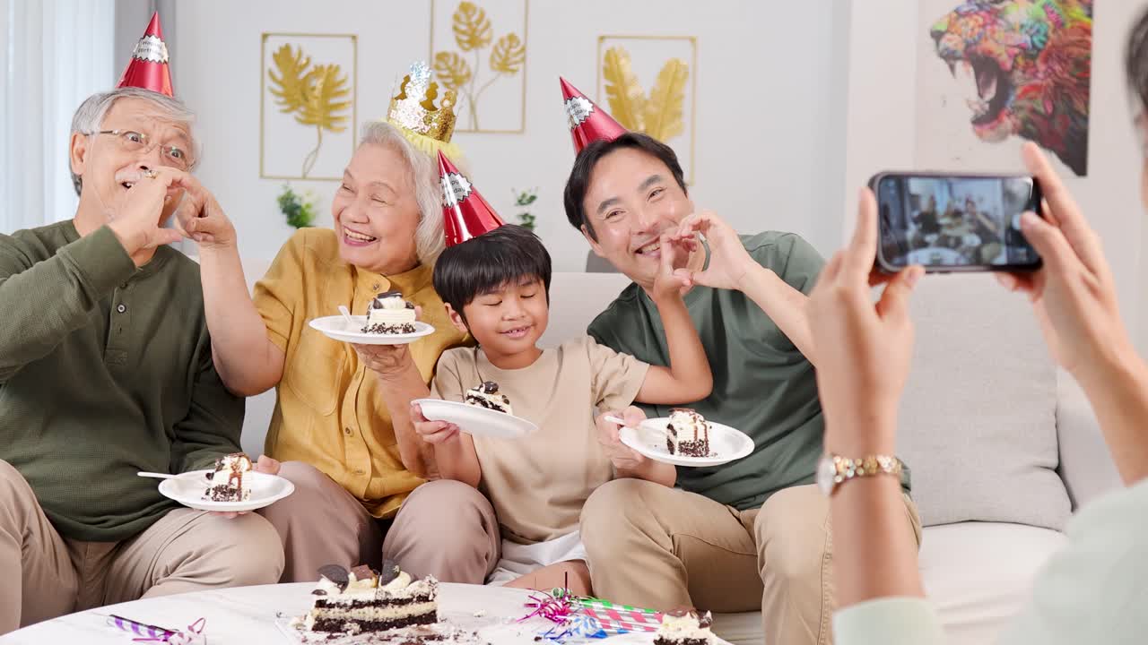 A joyful family celebrates a birthday, forming heart shapes with hands, captured in a bright, cheerful setting