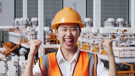 close up of asian female engineer with safety helmet standing and screaming goal celebrating working in the warehouse with shelves full of delivery goods