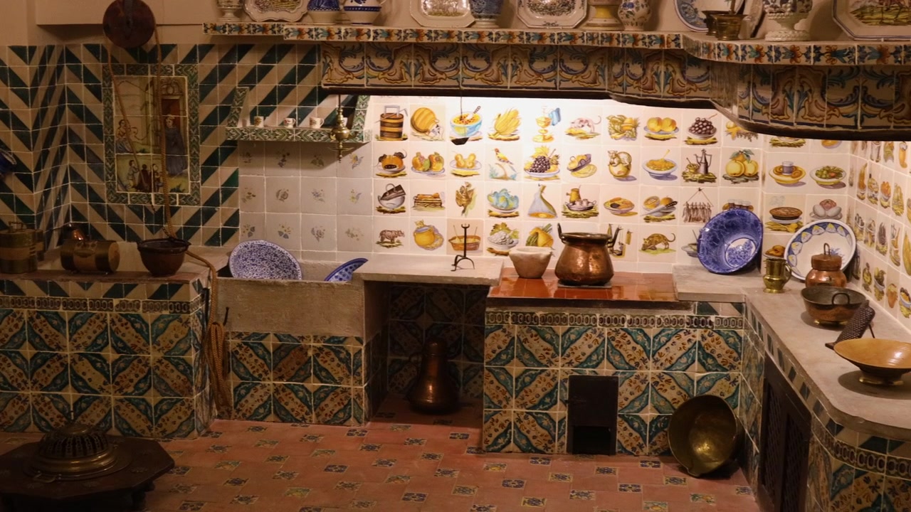 Cucina in miniatura riccamente decorata che espone ceramiche tradizionali, pentole in rame e motivi elaborati, evocando gli interni dei palazzi di un tempo