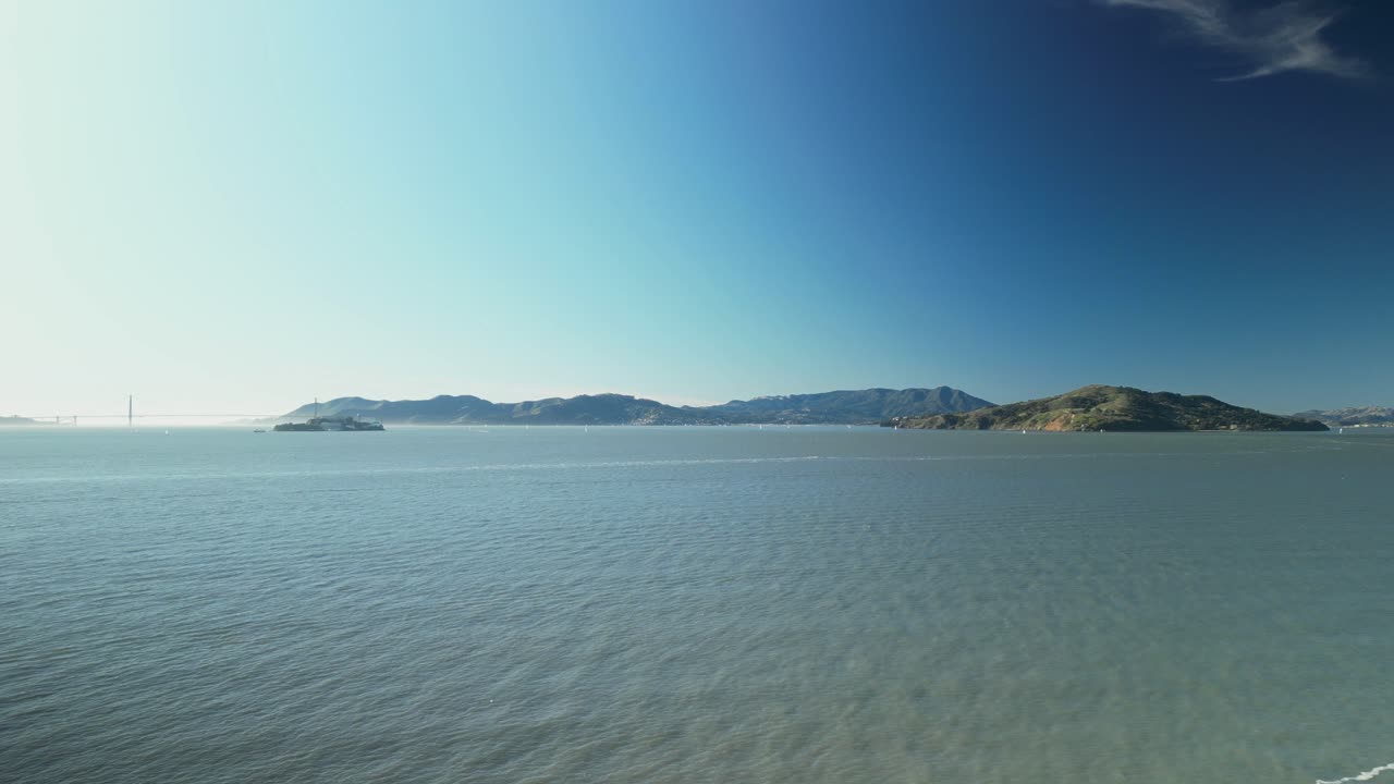 Aerial view of the calm sea stretching between San Francisco and Treasure Island, California, with sparkling waters reflecting the city skyline in the distance.