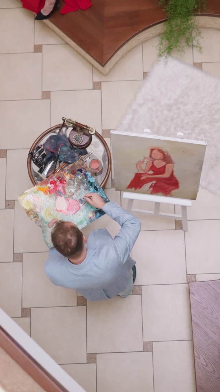 pintor prepara colores en la paleta en el taller. artista hábil combina pinturas para el dibujo de retratos de mujeres en la galería con plantas en olla. ocupación artística