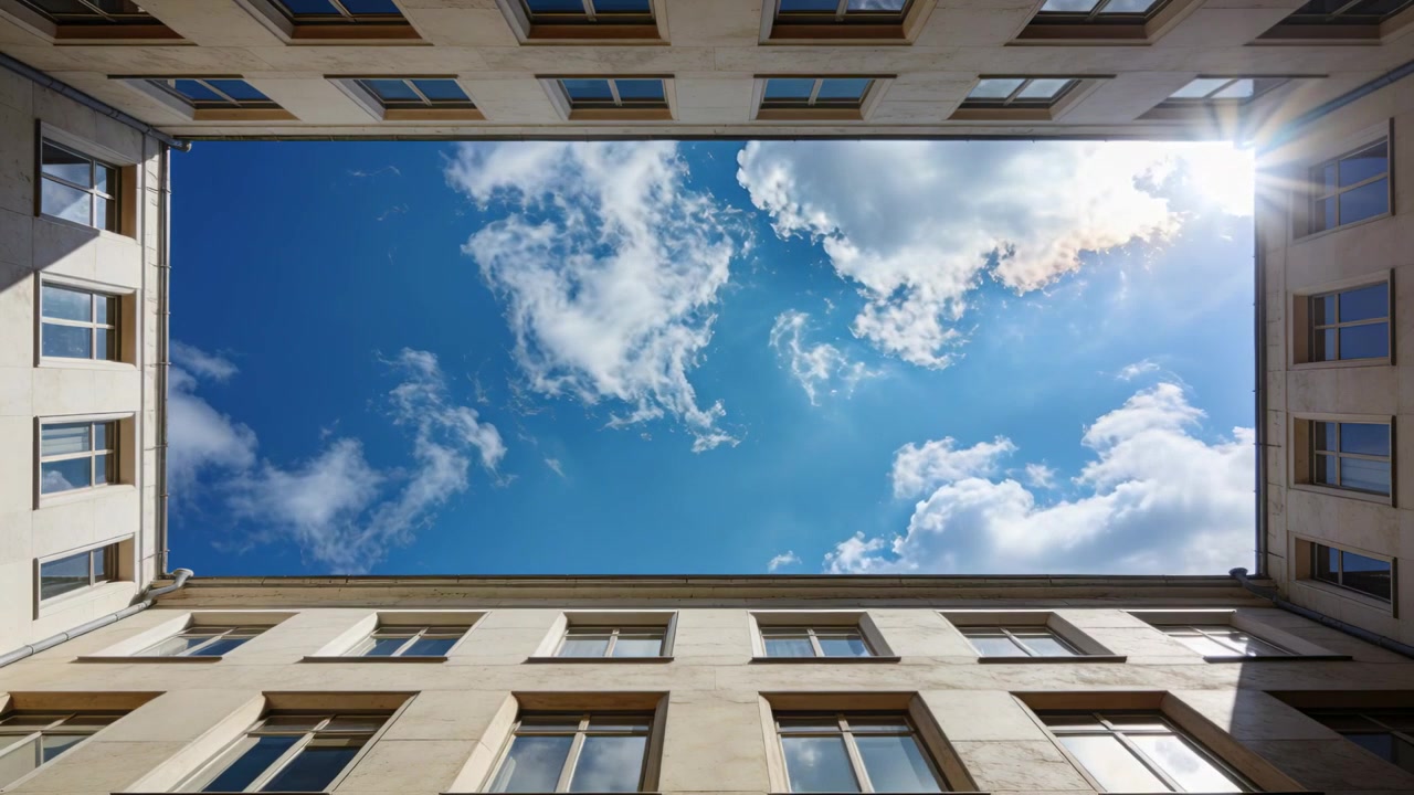 Vento che soffia che sposta le nuvole attraverso il cielo centrale incorniciato da muri beige in un cortile con il bagliore crescente.