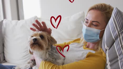Animation-of-heart-icons-over-caucasian-woman-with-face-mask-petting-dog