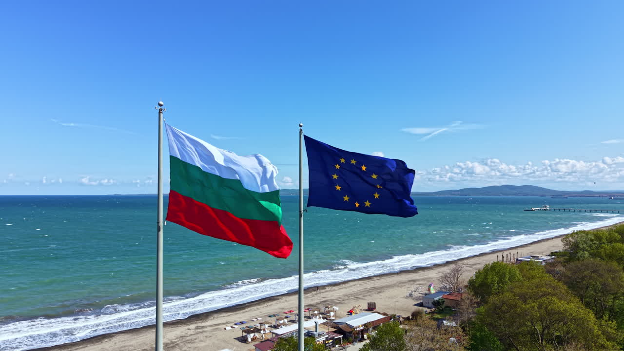 Due bandiere sventolano su aste in riva al mare, mostrando la bandiera bulgara e quella dell'Unione Europea, in una giornata limpida e soleggiata vicino alla spiaggia