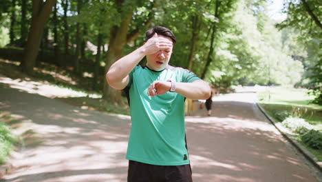 tired japanese runner fitness man using smartwatch bracelet watch checking result heartbeat in park