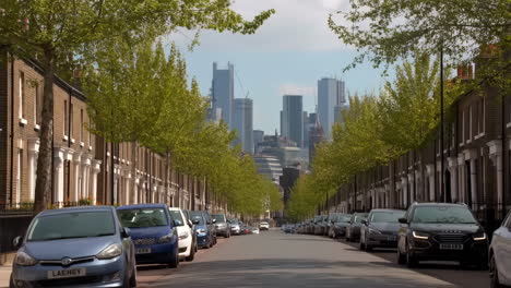 quiet residential street lined with cars and trees overlooking a city skyline