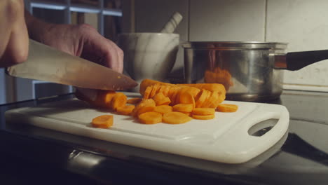 chopping carrots on cutting board with knife in kitchen, close-up