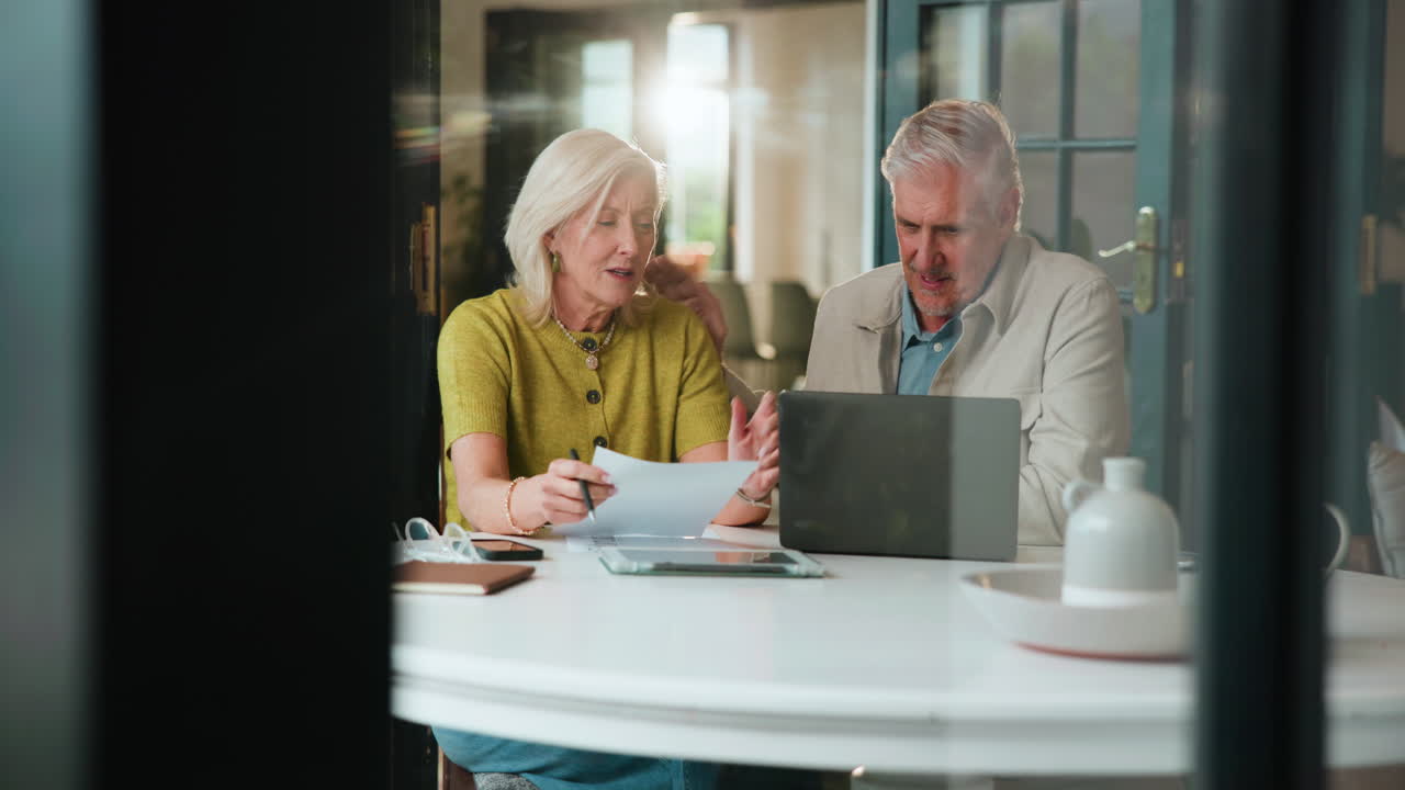 Eldre par diskuterer økonomi hjemme med bærbar PC og dokumenter