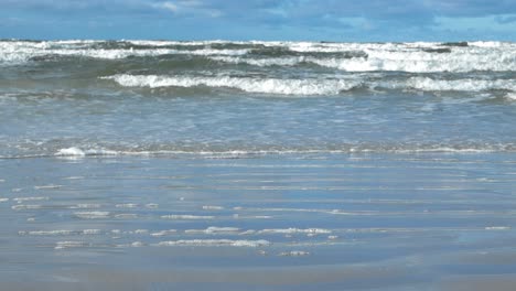 baltic ocean sea water waves coming to shore in slow motion with big waves, ripples and splashy white water leaving behind bubbles and foam on the sandy shoreline during day time in vääna jõesuu.