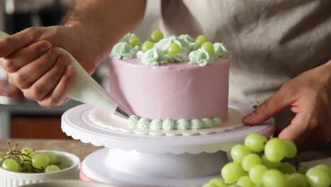 Man-decorating-a-cake,-using-a-white-cream-decoration-placer-making-round-circle-around-the-rotating-cake,-sweet-cake-preparation-concept