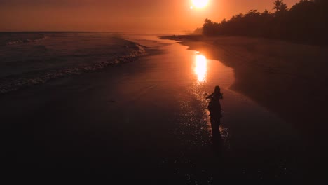 drone view of a woman riding motorcycle towards the sunset on the beach, riding in the water at pasut beach, bali indonesia