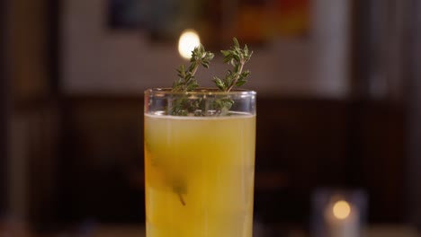 close up view of an orange cocktail with a thyme garnish in a japanese sushi restaurant with the video tilting up in slow motion