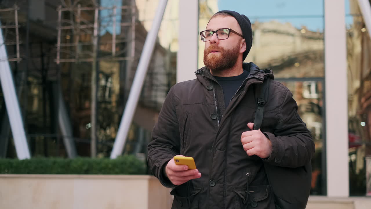Man with beard and glasses using smartphone in urban setting