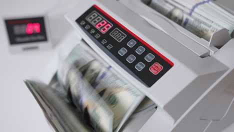 male hand inserts a wad of hundred dollar bills into a slot of cash counting machine. equipment for financial operations close up. blurred backdrop.