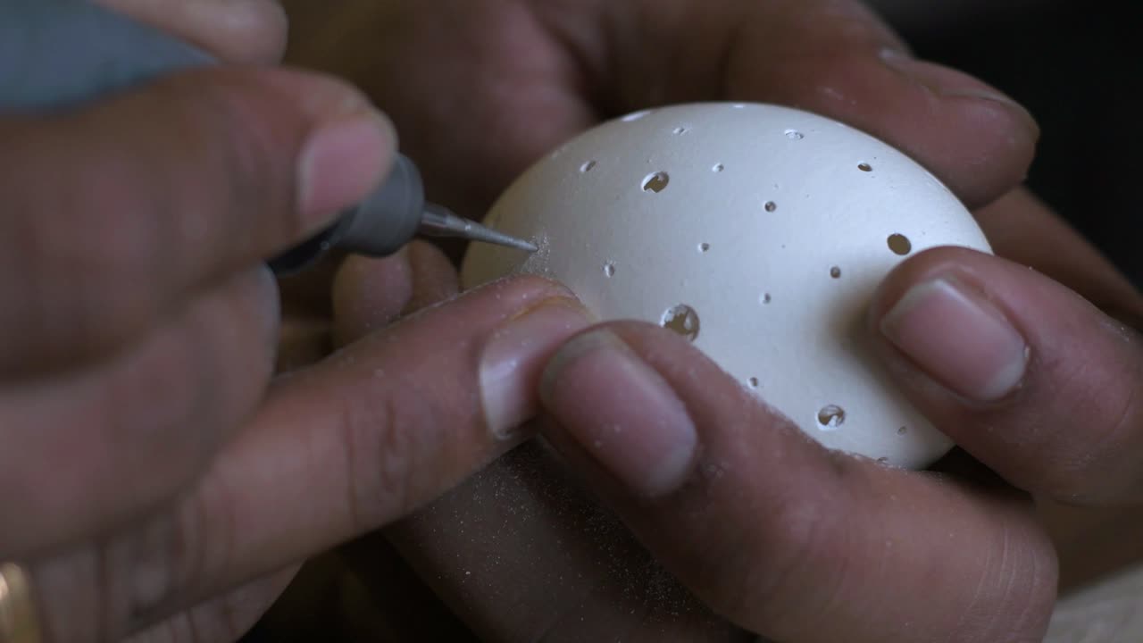 Closeup of a person carving chicken egg using a drill with bare hands