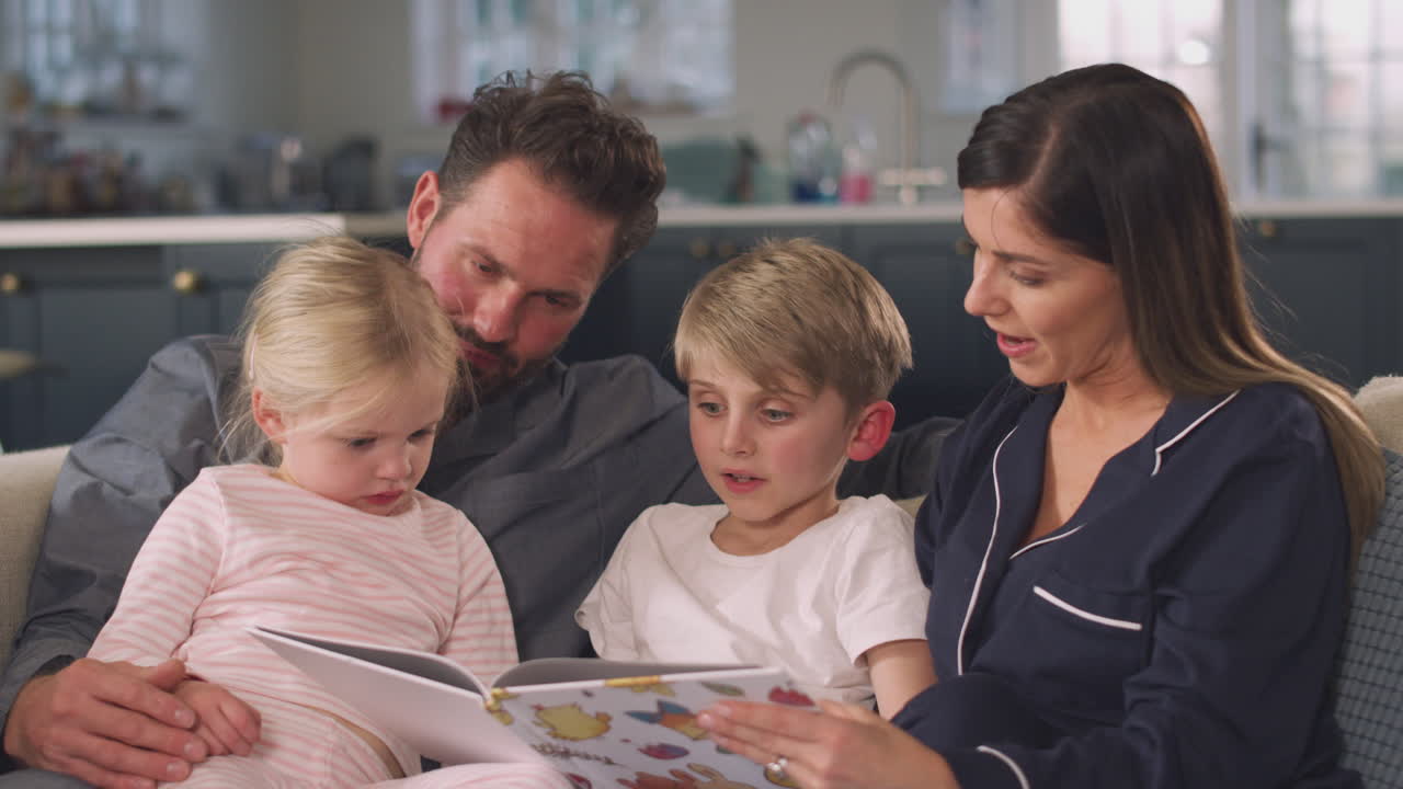 Famiglia sorridente seduta sul divano che legge insieme una favola della buonanotte da un libro.