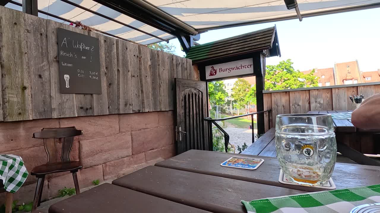 Hand lifts tall beer glass from wooden table at outdoor beer garden in Germany, daylight