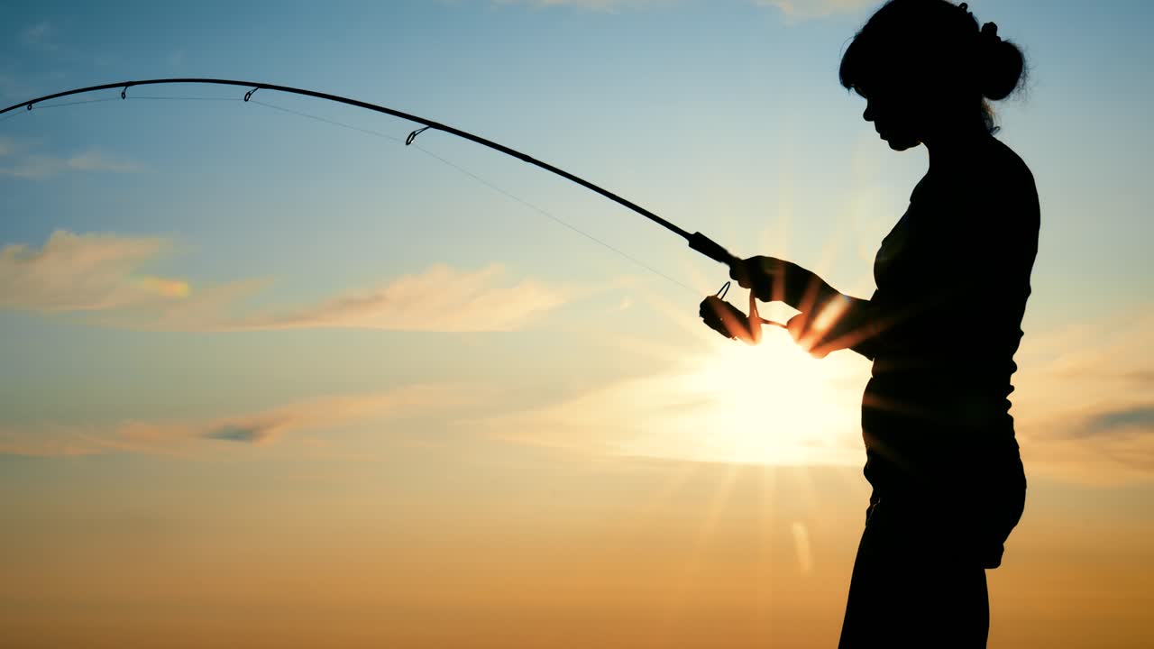 Seorang wanita memancing dengan joran pancing saat matahari terbenam. Wanita itu berhasil menangkap ikan, tetapi ikan tersebut lepas dari kail.