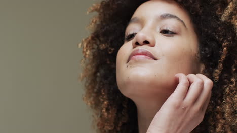 mujer biracial con cabello oscuro tocando la mejilla en fondo beige, cámara lenta