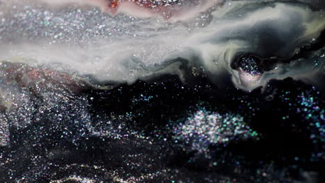 macro shot of black and grey glitter ink spreading through a milky liquid, pushed by injected air in a dynamic motion