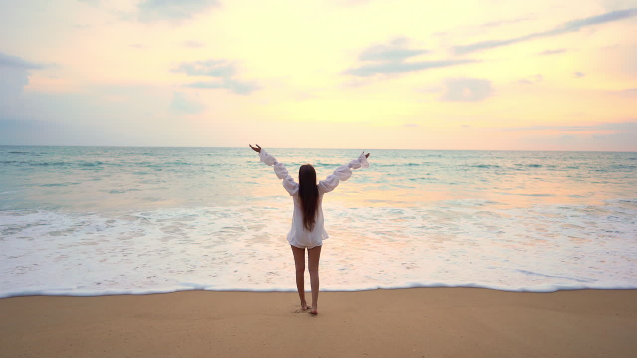 해변에서 팔을 들고 해질녘 지평선을 바라보는 여성의 뒷모습