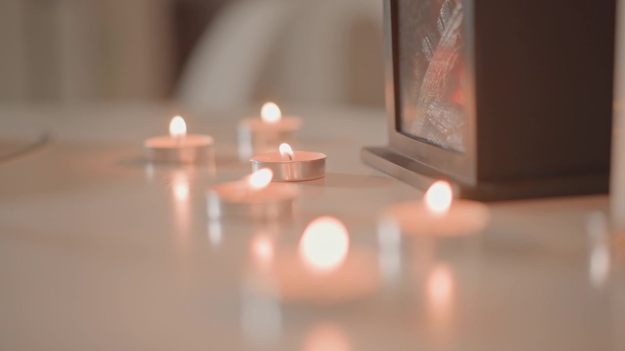 Vue en contre-plongée montrant des bougies chauffe-plat disposées sur une table lisse, les flammes centrales nettes tandis que les bougies proches et lointaines s'estompent dans un doux bokeh, créant une atmosphère intérieure chaleureuse et paisible.