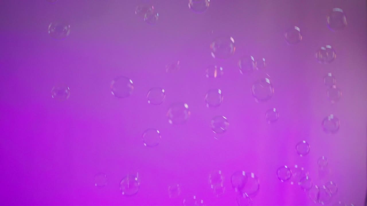 Static shot of bubbles with a purple wall behind it coming from up, indoor