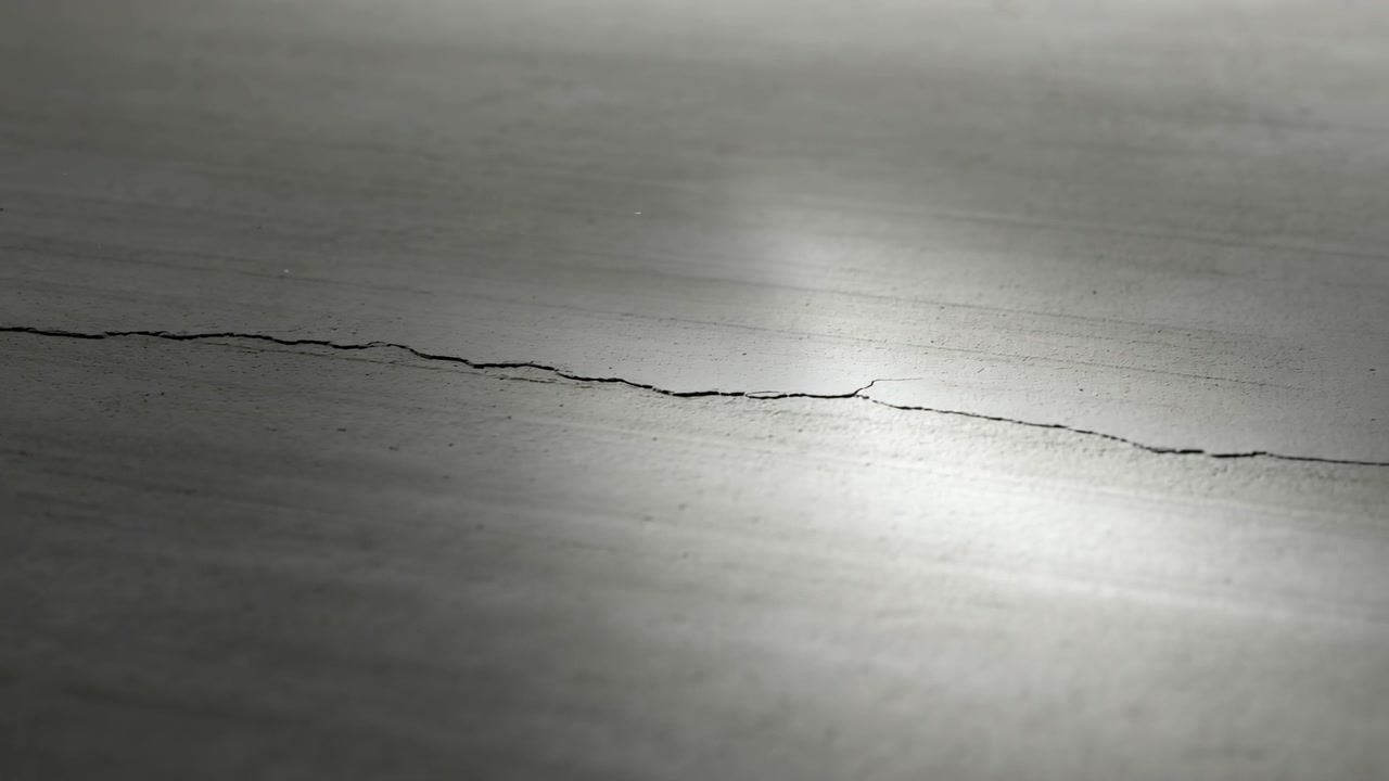 Close-up of a cracked wooden surface captured at the video midpoint, showing a fine fissure running across a smooth plank
