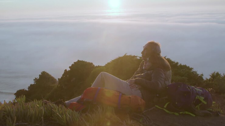 Homem e mulher alegres se abraçando, relaxando depois de uma caminhada, conversando e admirando a vista deslumbrante ao pôr do sol