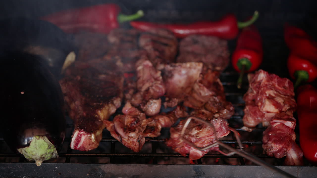 Daging panggang dengan bekas panggangan terlihat jelas sedang dibalik saat dimasak di atas bara api panas bersama sayuran.