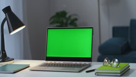 mesa de trabajo en el hogar, portátil con pantalla de clave croma, lámpara, gafas y libros, el hombre está encendiendo la lámpara de piso