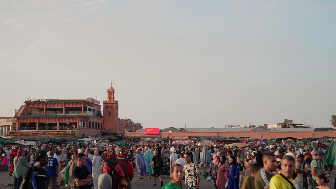 Bustling Marrakesh marketplace with a large crowd under a warm evening sky