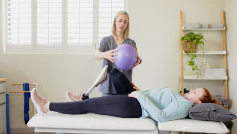 physical therapist with prosthetic leg helping patient with exercise ball therapy
