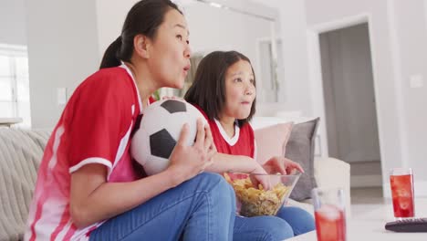 Video-De-Una-Feliz-Madre-Asiática-Y-Su-Hija-Comiendo-Papas-Fritas-Y-Viendo-Un-Partido-En-La-Televisión