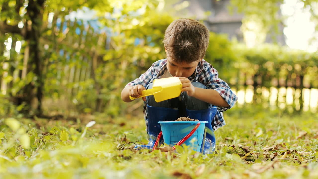un retrato de un niño haciendo jardinería. pone tierra con una pala en su cubo. fondo borroso