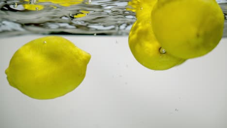 cuatro frutas cítricas de limón enteras cayeron en agua burbujeante fresca y limpia