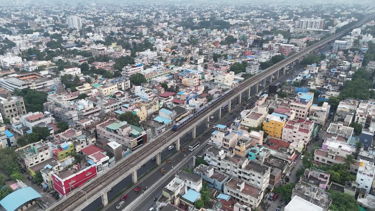 An aerial drone shot of a Chennai metro train passing through a busy city with traffic below.