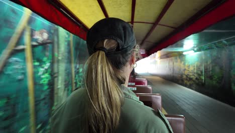 women riding on a small scenic train as it travels through a tunnel painted in murals