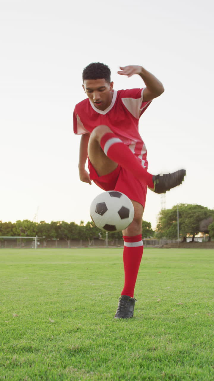 video vertical de un jugador de fútbol biracial en el campo pateando la pelota