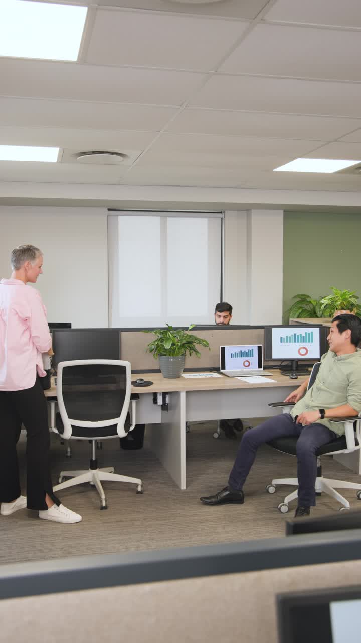 Video verticale: diversi colleghi che accolgono un collega che entra in ufficio, esaminando i grafici sui monitor