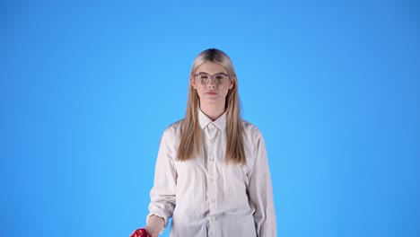 Junge-Kaukasische-Frau-Spielt-Und-Wirft-Einen-Ball-In-Weißem-Hemd-Und-Intelligenter-Brille,-Blonde-Nordische-Schöne-Frau,-Professioneller-Studio-Chroma-blauer-Hintergrund,-Oberkörper